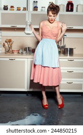 A Woman Is Standing In The Kitchen And Looks At The Floor. On The Floor, Spilled Milk.