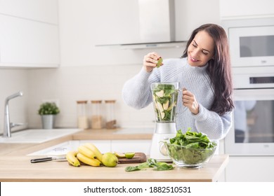 Woman standing in a kitchen squeezing lime into a blender full of fruit and vegetable.