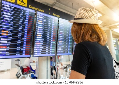 Woman standing and looking time board for flight schedule at airport.Travel planning vacation on holiday or summer concept.