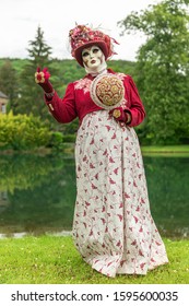 A woman standing in mask and red masquerade costume agains the pond background