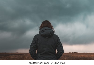 Woman standing in meadow, looking at the horizon and dark dramatic stormy clouds, rear view selective focus - Shutterstock ID 2108544668
