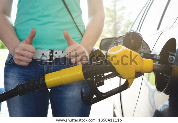 Woman is standing near a fuel\
nozzle and is showing a thumbs up. High quality fuel concept.\
