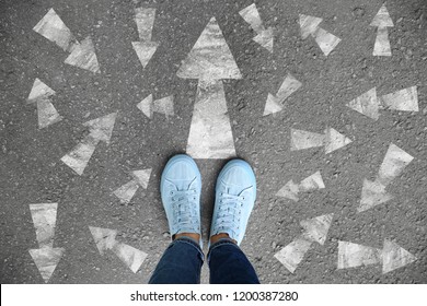 Woman Standing On Asphalt Road With Arrows Pointing In Different Directions. Concept Of Choice