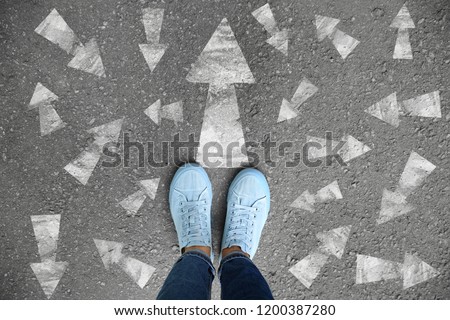 Woman standing on asphalt road with arrows pointing in different directions. Concept of choice