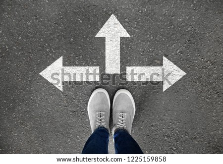 Woman standing on asphalt road with arrows pointing in different directions. Concept of choice