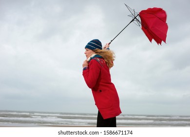 A woman standing on a beach with her umbrella blowing inside out - Powered by Shutterstock