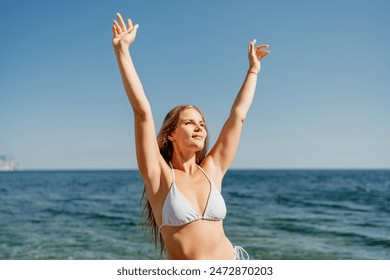 A woman is standing on the beach with her arms raised in the air - Powered by Shutterstock