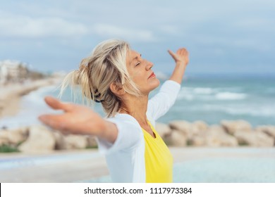 Woman standing on a beach meditating with outstretched arms, head back, eyes closed and a serene expression