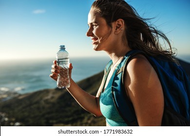 Woman standing on the cliff and drinking water. Female mountaineer looking at beautiful view with a water bottle in hand.