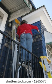 Woman Standing On Ladder Painting Exterior Of House