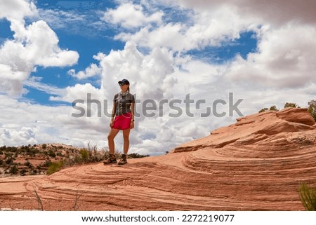 Woman standing on layered rock formation near Mesa Arch, Moab, Canyonlands National Park, Utah, USA. Sandstone buttes of petrified sand dunes. Outer layers stripped by erosion with folds and swirls