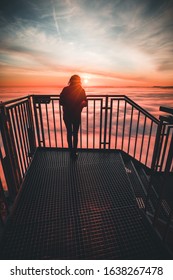 Woman Standing On Mountain Peak Watching Sunrise Over A Sea Of Fog