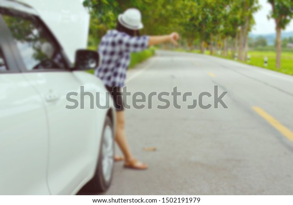  woman standing on the street hitchhiking,\
asking for help in case of a broken car The whole image is blurred\
for the background.