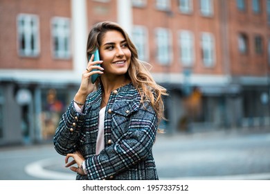 Woman standing on street and using mobile. Focus is on woman. 