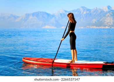 Woman standing on sup board and enjoying peace and quiet outdoors - Powered by Shutterstock