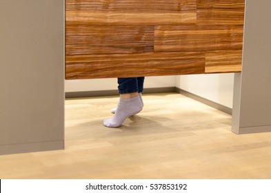 Woman standing on tip toe in a changing room at a store as she tries on clothes, view of her feet under the wooden door