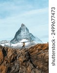 A woman standing on top of rocky mountain with iconic Matterhorn mountain on sunny day at Zermatt, Switzerland