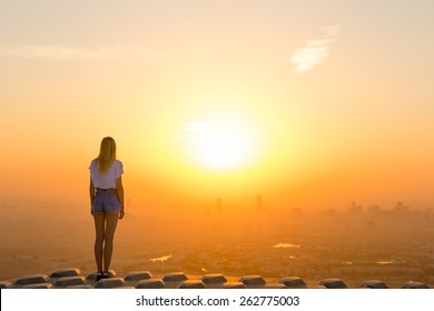 Woman Standing On Top Of Skyscraper Overlooking The City At Sunrise