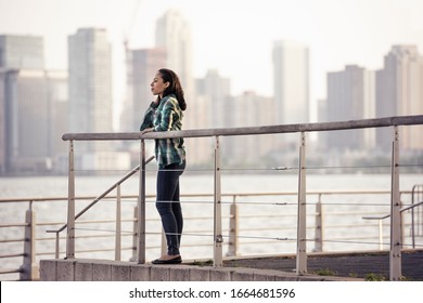 A Woman Standing On The Waterfront, View To The City Over The Water In New York City.