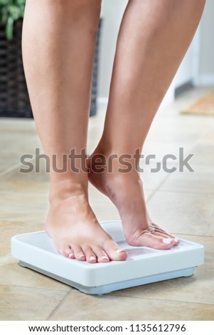 Woman Standing on Weight Scale At Home.