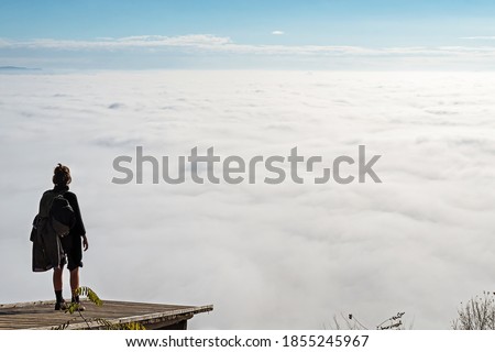 Woman standing on a wooden platform and enjoying the view of fog covered valley below. Hiking, achievement, expectation, optimism and self-reflection concepts.