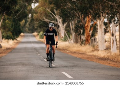 Woman Standing Out Of The Saddle On Road Bike While Riding. Pro Cyclist Exercising On Empty Road.