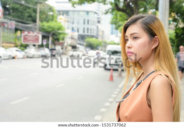 Woman standing side of the street\
waiting for taxi with down town road background in\
Thailand.