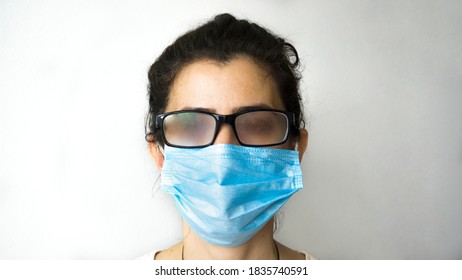 A Woman Standing With Smoky Glasses And A Mask On White Background. Female Can't See Because Of Her Breath Closing The Glasses.