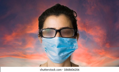 A Woman Standing With Smoky Glasses And A Mask On Sky Background. Female Can't See Because Of Her Breath Closing The Glasses.