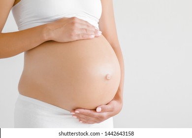 Woman standing and touching with hands her naked big belly. Isolated on gray background. Emotional loving pregnancy time - 37 weeks. Baby expectation. Love, happiness and safety concept. Closeup.