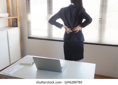 Woman Standing Touching Her Lower Back Part Feeling Painful After Sitting And Working At Her Desk For Long Time. Physical And Muscle Strain Need Relaxation And Stretching To Avoid Office Syndrome