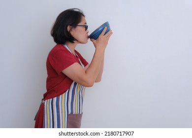 Woman Standing Wearing Apron Sipping A Bowl Of Soup 