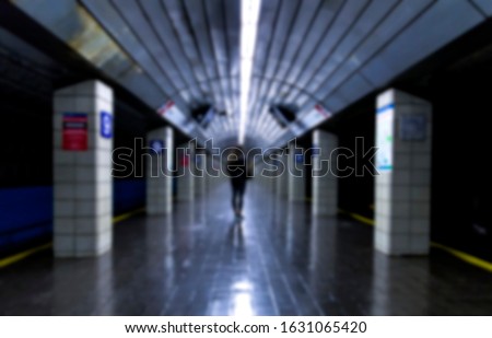 Woman stands alone in empty subway station with dark tones, blurred