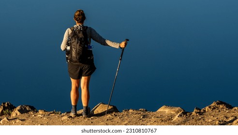 Woman Stands Along Edge of Rim Over Crater Lake with trekking pole - Powered by Shutterstock