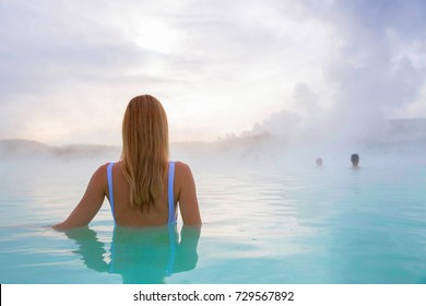 Woman stands back and enjoys spa in hot spring Blue Lagoon in Iceland. Early morning scenery