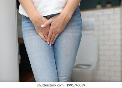 Woman stands in bathroom and covers her lower abdomen with her hand