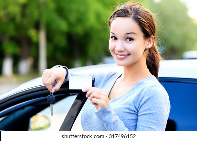 Woman stands beside a car and shows keys and white card