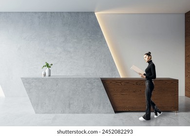 A woman stands by a modern reception desk in an office lobby with a gray background, showcasing a contemporary business interior - Powered by Shutterstock