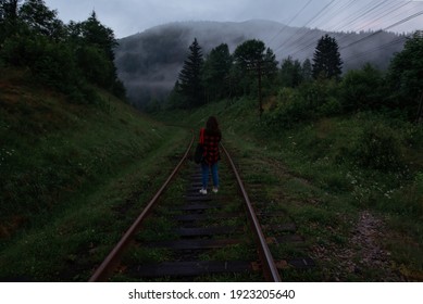 Woman stands in the evening on the railway track on the background of a misty beautiful mountain landscape. A tourist walks in the twilight on the railway track in the mountains. - Powered by Shutterstock