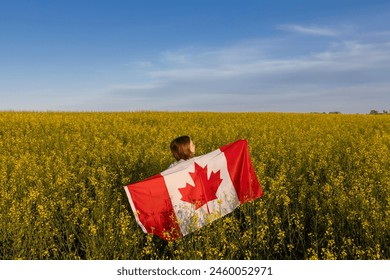 woman stands with her back among a yellow, flowering rapeseed field and proudly holds a large Canadian flag on a sunny day. Canadian Independence Day. freedom, trust, pride, national symbol - Powered by Shutterstock