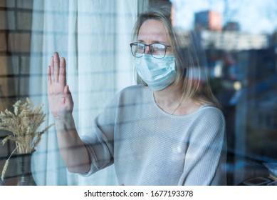 woman stands and looks out the window, self-isolation, prevention of corona virus