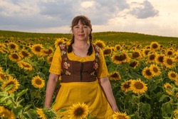A Woman Stands In The Middle Of A Field With Many Yellow Sunflowers. Her Hair Is Braided, Dressed In German National Clothes. Sunny, Summer Day