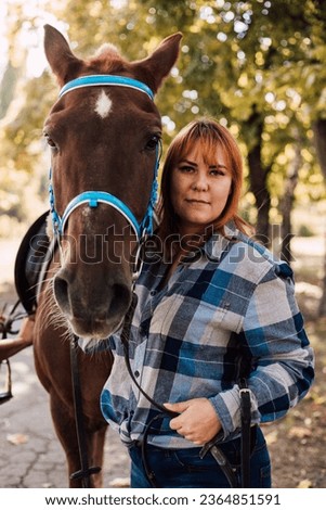 A woman stands near a horse. Farming, horseback riding. Autumn Park. High quality photo