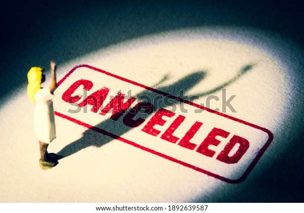 Woman stands on cancelled stamp with dark shadow.\
Person is labelled or stereotyped. Cancel culture concept with\
noise and grain and select\
focus.
