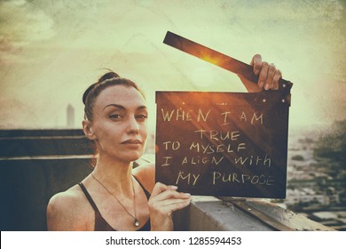 The woman stands on the roof with a poster "When I am true to myself,
I align with my purpose" International Womens Day  concept. 