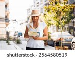 Woman stands on a sidewalk holding a map, observing the surroundings in a vcity. 