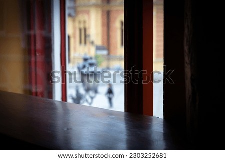 A woman stands on the street, view from behind a shuttered window.