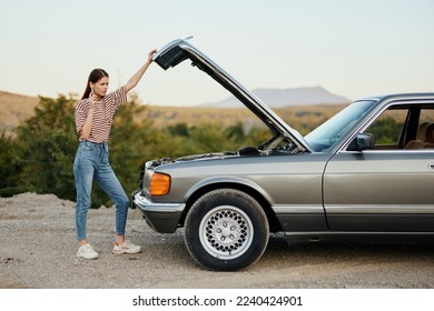 A woman stands outside a broken-down, dangerous old car with the hood open with a wrench on a road trip alone - Shutterstock ID 2240424901