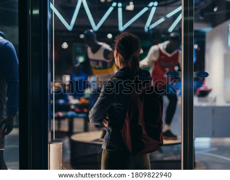 Woman stands outside the store and looks inside through the window.