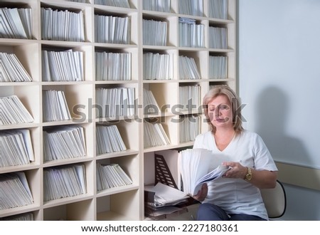 A woman stands with a stack of documents at a shelf with cells. The concept of a polyclinic registry employee